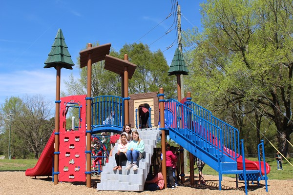 Students playing on the playground. Three sitting on steps of play structure.