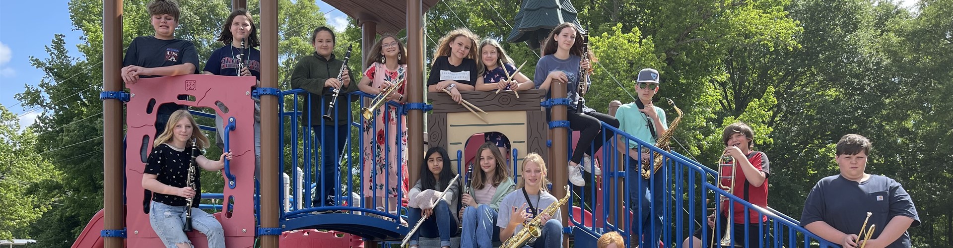 Students holding band instruments while standing on playground equipment